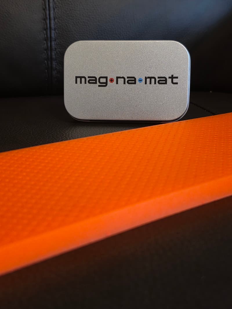 The mag·na·mat v1.0 branded metal tin on orange build surface.